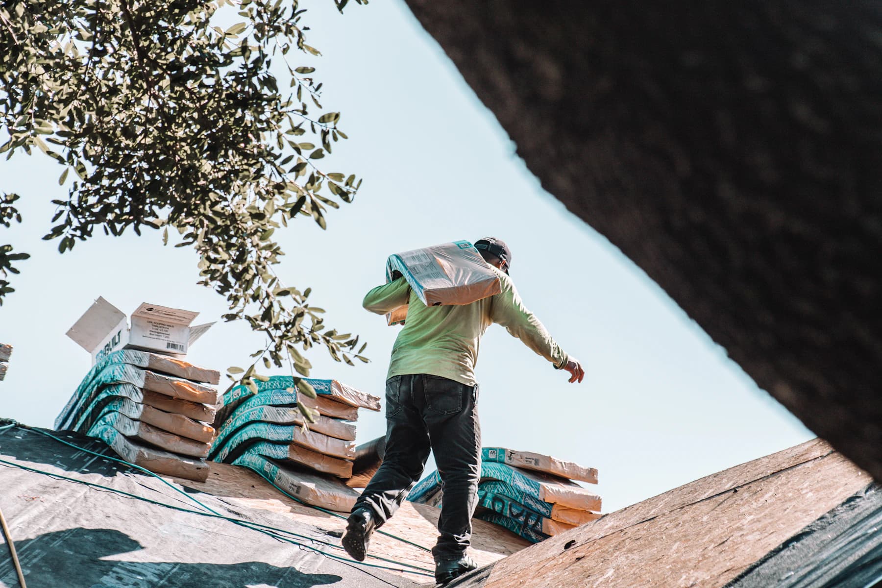 A roofer carrying a bundle of shingles across a roof deck
